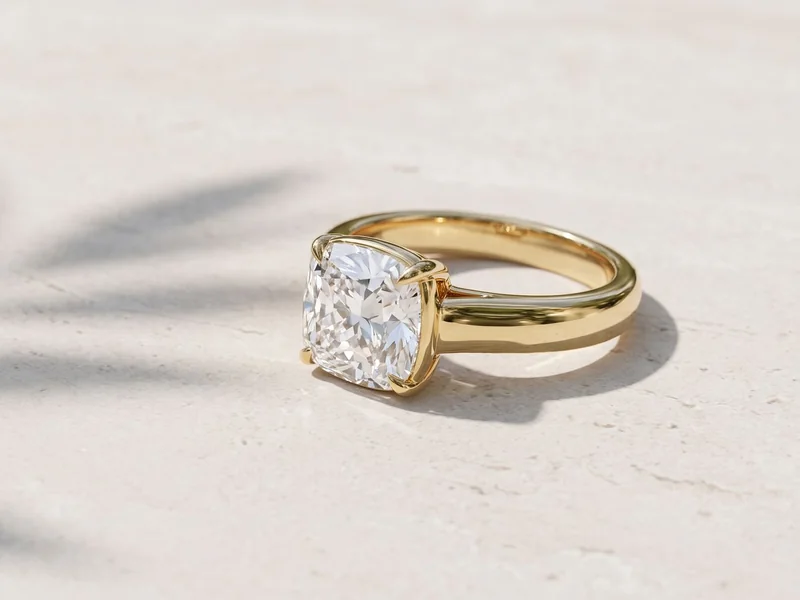 Levendi Jewellers homepage hero image: Wave of Love cushion cut four claw engagement ring in yellow gold on pale stone