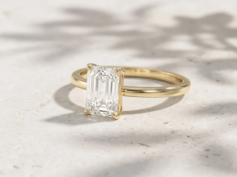 Levendi Jewellers homepage hero image: Classic emerald cut plain band engagement ring on pale stone